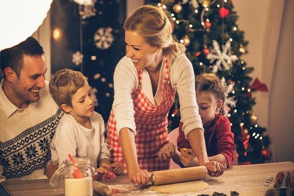 Family baking cookies for Christmas together, mother rolling dough, children helping their mother.
