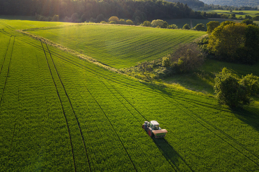 Aerial view on agricultural landscape in spring. A farmer with his machine is driving on a wheat field. Captured with a drone in southern Germany.