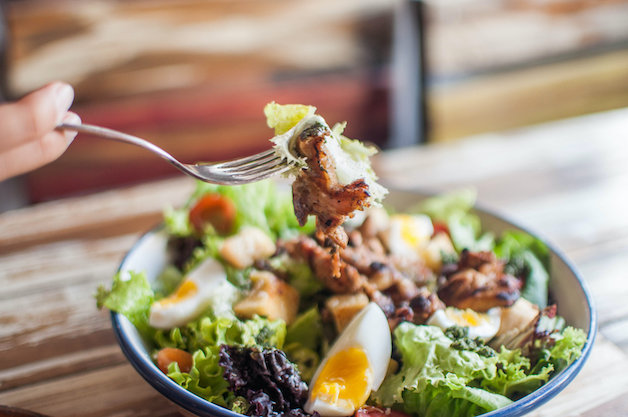 A high-angle close-up view of a salad in a bowl on the wooden table in a restaurant during daytime